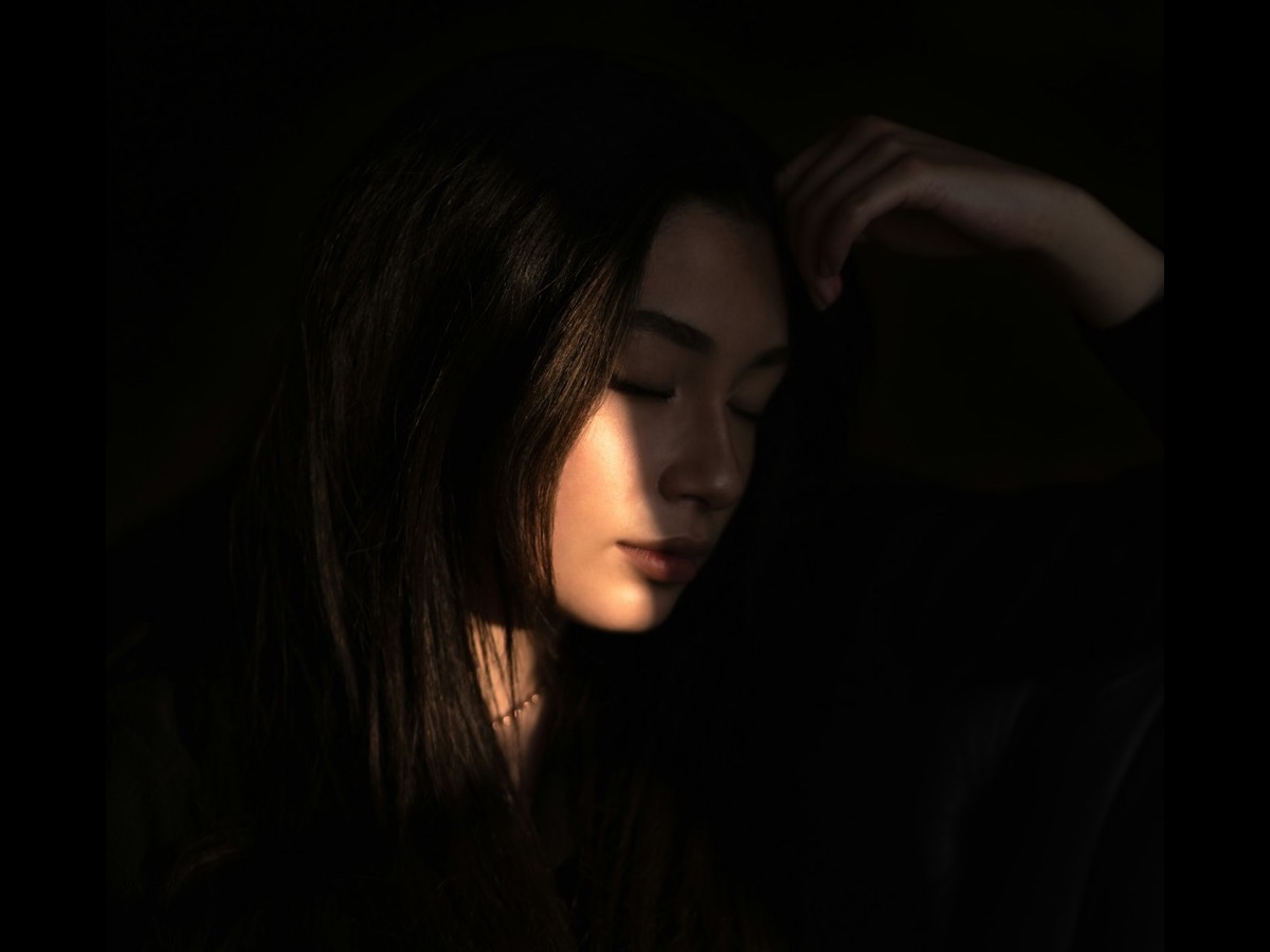 A woman in a Copenhagen apartment beside a large window, hands wrapped around a cup.