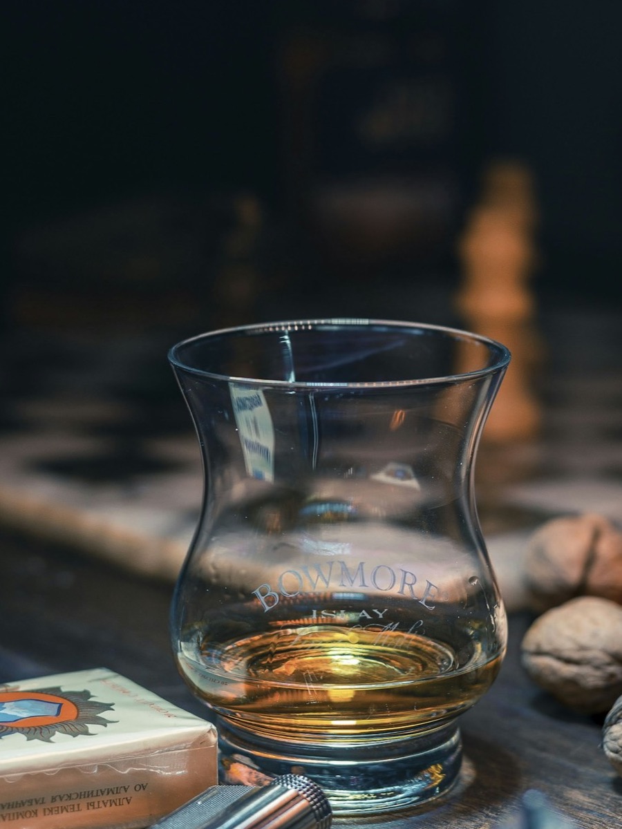 A cut-glass whiskey tumbler with amber liquid, lit from behind.