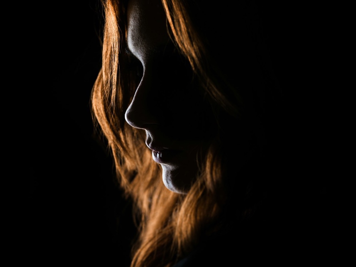 A woman in a black dress at a hotel bar, half-lit by a candle.