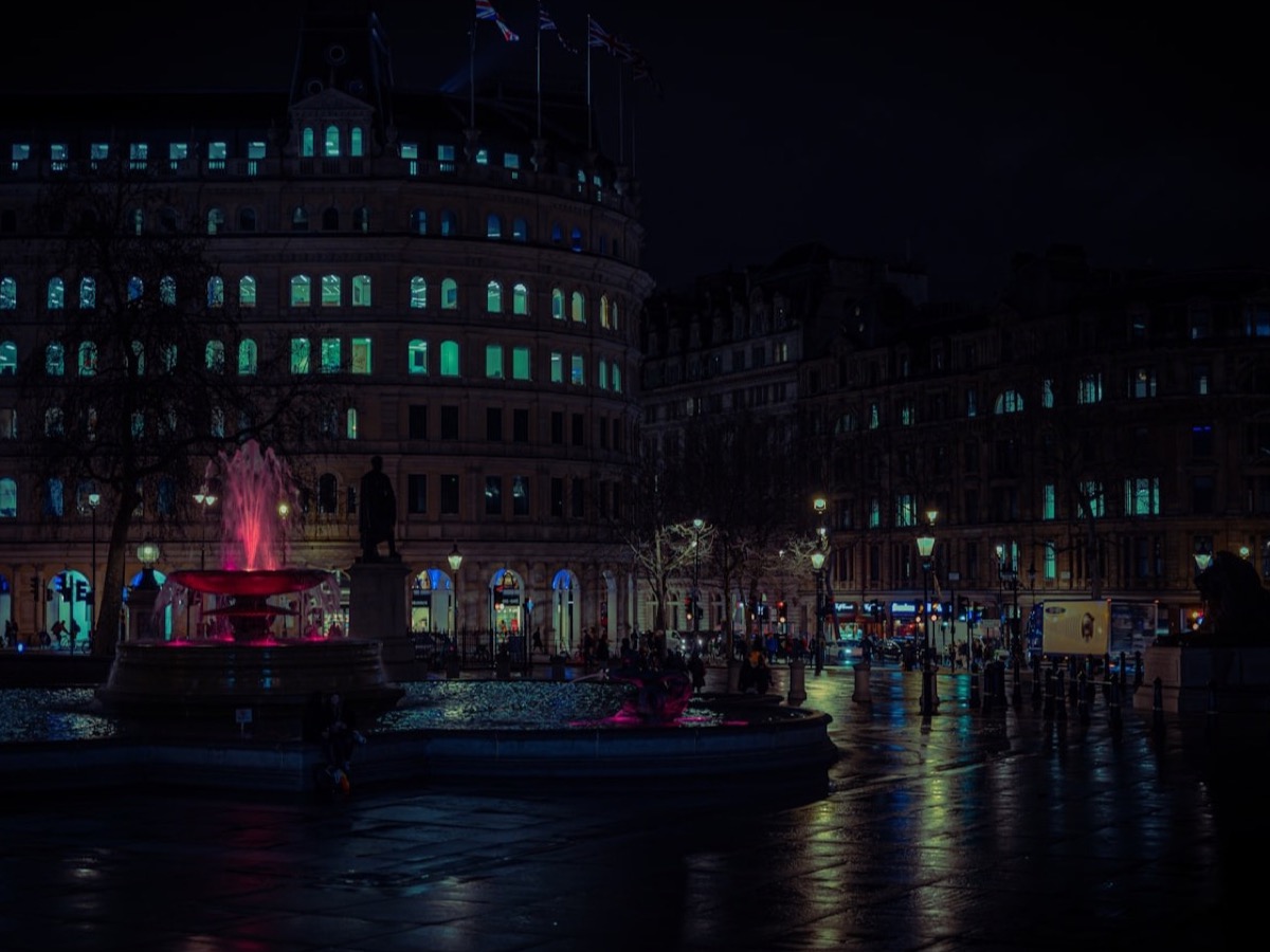 A woman walking through neon-lit rain, holding an umbrella, from behind.